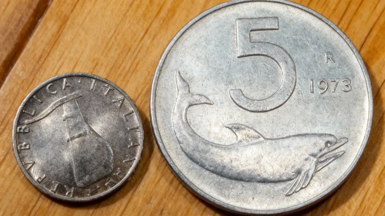Primo piano di una moneta da 5 lire italiane con un delfino accanto a un'altra moneta