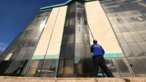 Persona che pulisce i vetri di un edificio alto utilizzando un'asta telescopica da terra