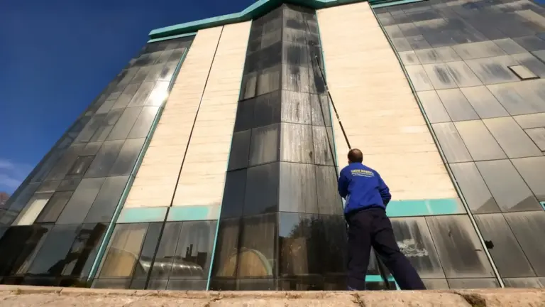 Persona che pulisce i vetri di un edificio alto utilizzando un'asta telescopica da terra