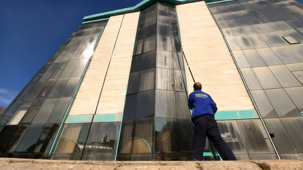 Persona che pulisce i vetri di un edificio alto utilizzando un'asta telescopica da terra