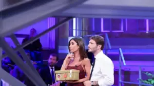 Due persone su un set televisivo di Affari Tuoi, una tiene in mano un pacco dorato