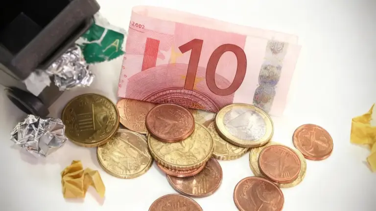 Monete e una banconota da 10 euro vicino a un piccolo bidone della spazzatura con rifiuti