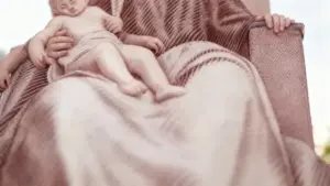 Statua di una figura seduta con un bambino in braccio, scolpita con dettagli morbidi